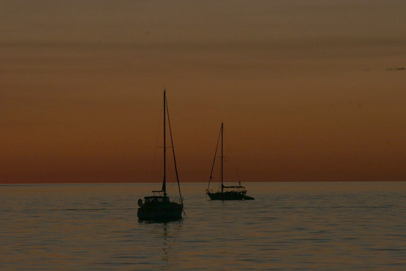 Sunset over water with distant sailboats
