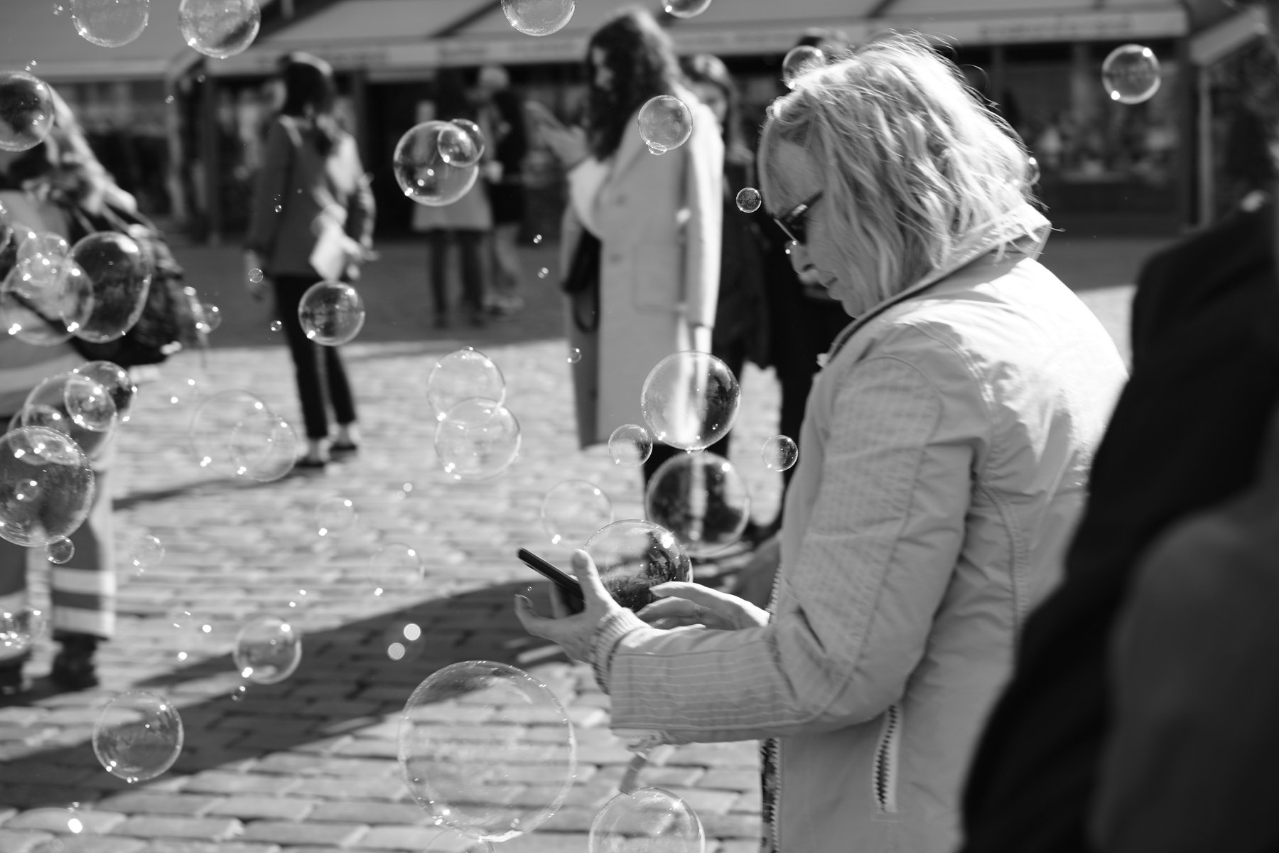 Black and white photo of a woman blowing soap bubbles in a crowd