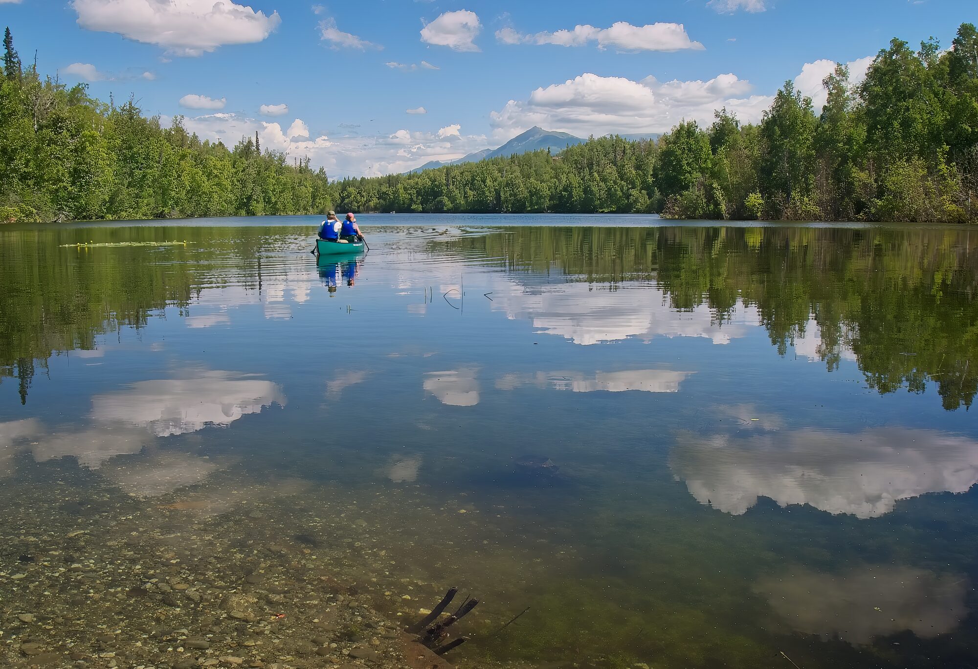 A dead-calm lake reflecting clouds with a single canoe in the middle
