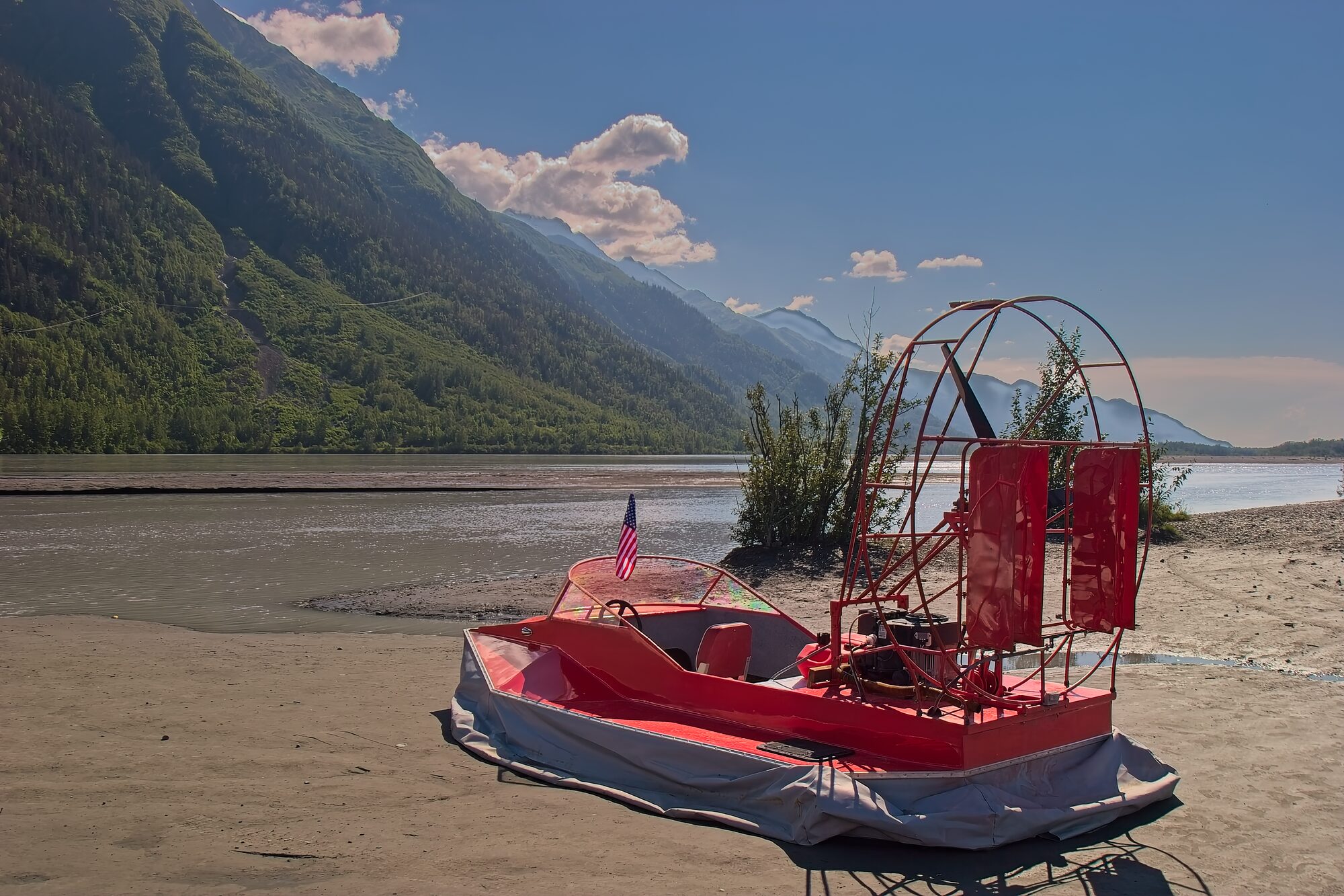 A red airboat resting on the braided sand of the Knik River flats