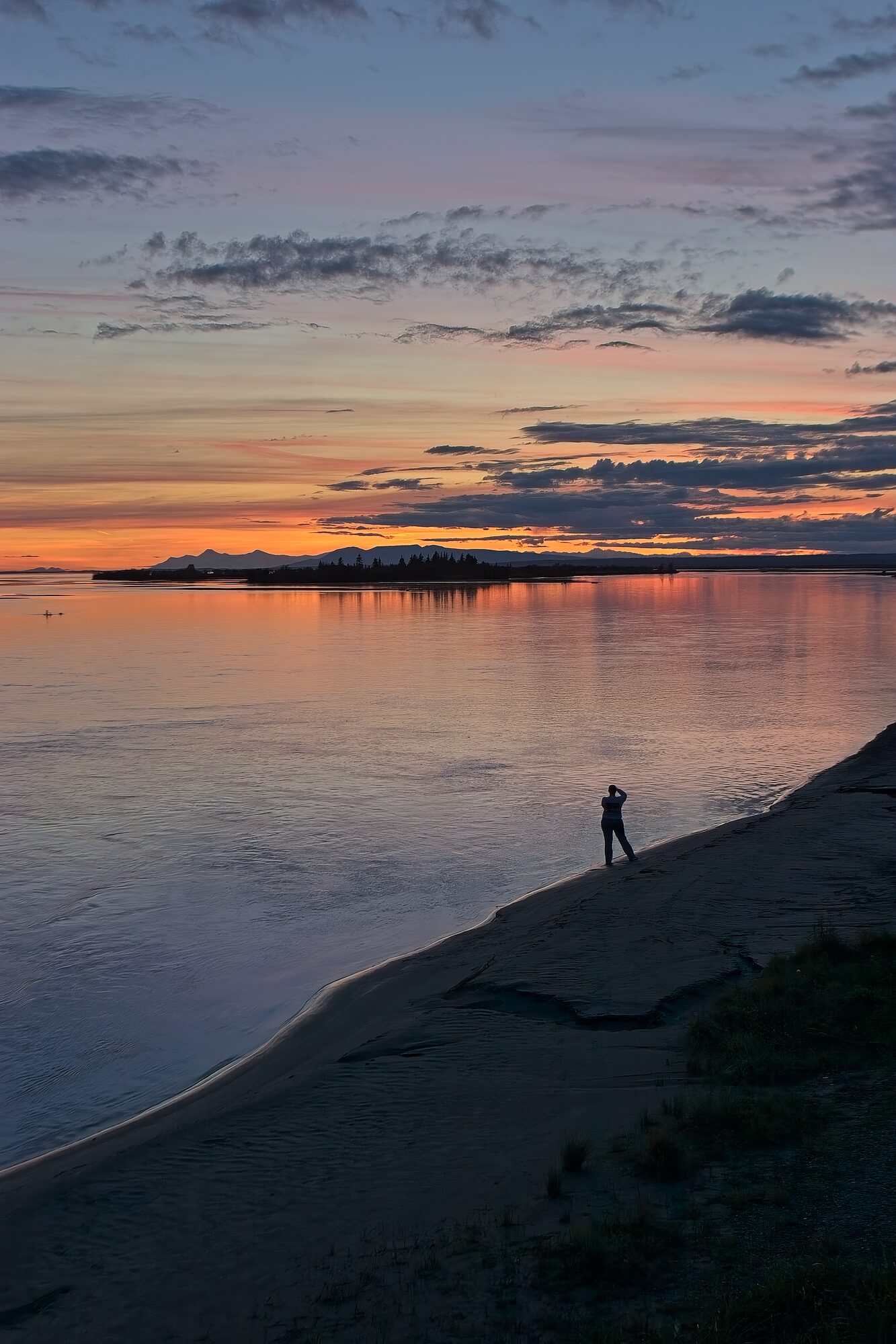 A lone figure on a river bar at dusk with Sleeping Lady mountain on the horizon
