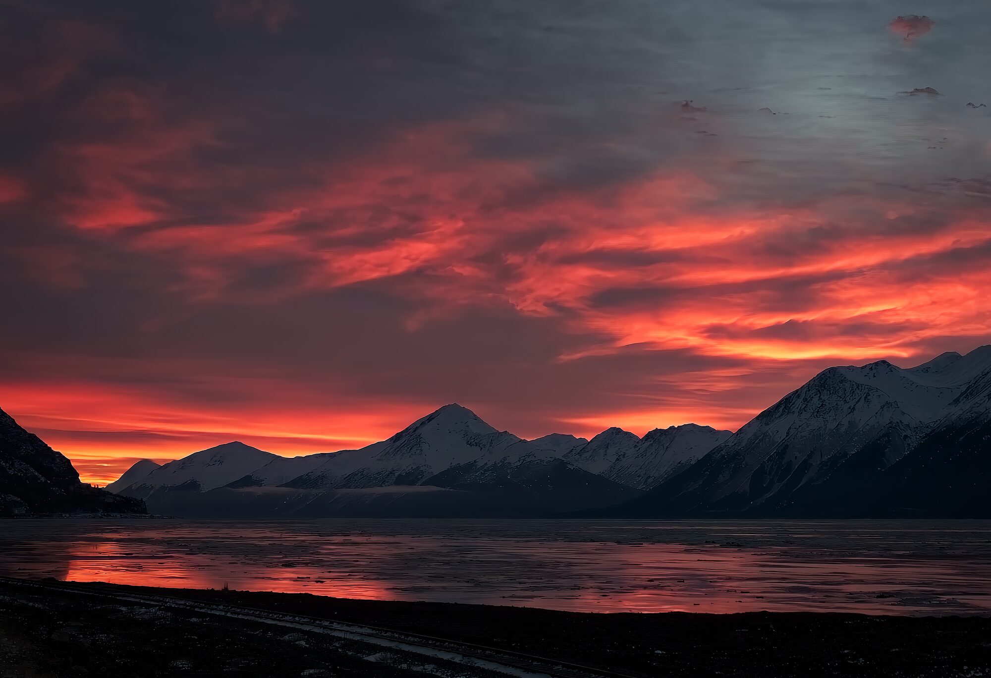 A fiery winter sunset over the snow mountains and open water of Turnagain Arm