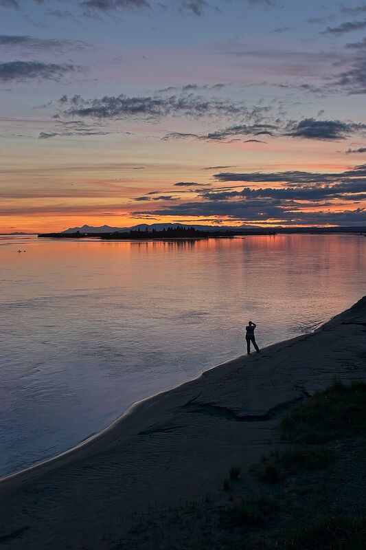 A lone figure on a river bar at dusk with Sleeping Lady mountain on the horizon